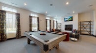 Located at 2845 Austin Manor Boulevard in Columbus, Ohio, this single-floor community clubhouse offers a thoughtfully designed amenity space built for both relaxation and entertainment. The welcoming entrance lobby features soaring ceilings, polished concrete flooring, and a mix of seating areas alongside a glass-enclosed private office or meeting room, providing a refined and functional first impression.

The open-concept lounge and game room serve as the heart of the space. A cozy seating area is anchored by a sleek, tile-surround fireplace flanked by industrial-style wood shelving units, with a wall-mounted television above. Plush sofas and accent chairs in rich tones of brown, blue, and red create an inviting atmosphere, complemented by large windows with decorative drapes that allow natural light to fill the room. Adjacent to the lounge, a full-size billiards table provides a focal point for recreation and social gatherings.

The gourmet-style kitchen is outfitted with bold dark cabinetry, crisp white quartz countertops, and a generous island with bar seating. Elegant globe pendant lights add warmth overhead, while stainless steel appliances and ample counter space make this kitchen well-suited for hosting events. Throughout the space, recessed lighting, neutral walls, and a cohesive modern design aesthetic create a polished and welcoming environment.