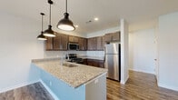 Located at 200 Jr Achievement Dr in Elkhart, Indiana, this single-floor residence offers a well-designed, open-concept layout with modern finishes throughout. The kitchen serves as a central focal point, showcasing rich dark-stained cabinetry, light granite countertops, and a full suite of stainless steel appliances including a gas range, over-the-range microwave, and refrigerator. A kitchen island with an undermount sink and pendant lighting above provides additional workspace and a casual dining option. Durable hardwood-style flooring runs throughout the main living areas, complementing the neutral gray walls and clean white trim. The living area is bright and open, benefiting from natural light and a ceiling fan, with French doors leading to a private balcony that offers outdoor views. The bedrooms are carpeted for comfort, each equipped with a ceiling fan and ample natural light. One bedroom includes a walk-in closet, providing generous storage. The bathroom features a granite-topped vanity with a dark wood cabinet, wood-look tile flooring, and a glass-enclosed walk-in shower. Overall, the unit presents a clean, contemporary aesthetic with thoughtful finishes and functional design throughout.