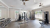 Located at 3785 Ladson Rd in North Charleston, SC, this fitness center offers a thoughtfully designed exercise space ideal for a comprehensive workout experience. The room features durable rubber flooring throughout, providing both safety and comfort during training sessions. Crown molding and neutral gray walls give the space a polished, upscale aesthetic that sets it apart from a typical gym environment.

Natural light floods the room through multiple white-framed windows, offering views of the surrounding outdoor area and creating a bright, inviting atmosphere. Large wall-mounted mirrors amplify the sense of space and allow users to monitor their form during exercise. Ceiling fans with recessed lighting keep the environment comfortable and well-lit.

The fitness center is comprehensively equipped for both strength and functional training. A multi-station cable machine and a selection of selectorized strength equipment support targeted muscle training, while a full rack of dumbbells accommodates a wide range of free weight exercises. Functional training tools include a dedicated rig loaded with stability balls, battle ropes, TRX suspension trainers, medicine balls, and resistance bands. Adjustable benches and a flat bench round out the strength training options. A wall-mounted television provides entertainment during workouts. The space is efficiently organized to maximize usability within its compact footprint.