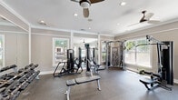 Located at 3785 Ladson Rd in North Charleston, SC, this fitness center offers a thoughtfully designed exercise space ideal for a comprehensive workout experience. The room features durable rubber flooring throughout, providing both safety and comfort during training sessions. Crown molding and neutral gray walls give the space a polished, upscale aesthetic that sets it apart from a typical gym environment.

Natural light floods the room through multiple white-framed windows, offering views of the surrounding outdoor area and creating a bright, inviting atmosphere. Large wall-mounted mirrors amplify the sense of space and allow users to monitor their form during exercise. Ceiling fans with recessed lighting keep the environment comfortable and well-lit.

The fitness center is comprehensively equipped for both strength and functional training. A multi-station cable machine and a selection of selectorized strength equipment support targeted muscle training, while a full rack of dumbbells accommodates a wide range of free weight exercises. Functional training tools include a dedicated rig loaded with stability balls, battle ropes, TRX suspension trainers, medicine balls, and resistance bands. Adjustable benches and a flat bench round out the strength training options. A wall-mounted television provides entertainment during workouts. The space is efficiently organized to maximize usability within its compact footprint.