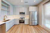 Located at 5301 W Tyson Ave in Tampa, FL, Unit 448 is a thoughtfully designed 610-square-foot studio apartment spread across a single floor. The open-concept living and kitchen area features warm light wood flooring, crisp white walls, and recessed lighting complemented by a modern ceiling fan, creating a bright and airy atmosphere. The well-appointed kitchen is equipped with stainless steel appliances — including a French door refrigerator, range, over-the-range microwave, and dishwasher — paired with light gray shaker-style cabinetry, a subway tile backsplash, and ample counter space. The bathroom offers a clean, contemporary aesthetic with a glass-enclosed walk-in shower featuring white subway tile surround, a vanity with storage, and light wood-look tile flooring that ties the space together cohesively. The private balcony, accessed through the main living area, features a sleek dark metal railing and provides open views of the surrounding community, palm trees, and blue Florida skies — an ideal outdoor retreat. The unit's modern finishes, efficient layout, and indoor-outdoor connectivity make it a practical and stylish living space in South Tampa.