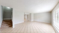 This two-story home offers a well-organized layout across two evenly sized floors, accommodating three bedrooms and two full bathrooms. The ground floor features a spacious living room finished with light-toned ceramic tile flooring and a textured ceiling, creating a bright, open atmosphere. Large windows allow natural light to fill the space, offering views of the surrounding exterior. The kitchen is equipped with dark cabinetry, a double-basin sink, white appliances including an electric range and dishwasher, and ample upper and lower cabinet storage. A dedicated laundry room with washer and dryer hookups provides added convenience on the main level. A hallway connects the ground floor spaces and leads to the staircase. Upstairs, the three bedrooms are carpeted for comfort, each featuring ceiling fans with light fixtures and closet space. The generously sized primary bedroom offers a comfortable retreat. Both bathrooms are finished with clean white fixtures, vanity storage, and a mix of tile and wood-look flooring. The textured ceilings are consistent throughout, contributing to a cohesive aesthetic. The layout is practical and functional, offering clearly defined living, sleeping, and utility spaces across both levels.