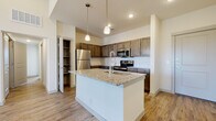 This well-designed single-floor residence offers a thoughtfully planned open-concept layout that seamlessly connects the kitchen and living areas. The kitchen serves as the centerpiece of the space, showcasing a large granite-topped island with an integrated sink and a sleek pull-down faucet, illuminated by elegant pendant lighting. Rich, dark-toned cabinetry lines the walls, providing generous storage, while a classic white subway tile backsplash adds a clean, timeless contrast. A full suite of stainless steel appliances — including a refrigerator, range, and over-the-range microwave — completes the culinary space. Light-toned wood-look flooring flows throughout the main living areas, enhancing the sense of openness and warmth. A walk-in pantry or storage closet is conveniently accessible from the kitchen. The bedroom features plush carpeting and a well-sized closet with a clothing rod. The bathrooms are finished with crisp white subway tile — one offering a glass-enclosed walk-in shower, and another featuring a soaking tub. Natural light filters in through windows, brightening the interior and contributing to an overall clean, contemporary ambiance throughout the space.