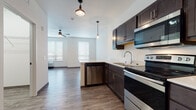 Located at 6824 University Avenue in Middleton, Wisconsin, this single-floor unit offers a thoughtfully designed, open-concept layout that seamlessly connects the kitchen and living areas. The kitchen is a standout feature, equipped with a full suite of stainless steel appliances including an electric range, microwave, refrigerator, and dishwasher. Rich, dark espresso cabinetry provides ample storage and contrasts beautifully with the light countertops, while pendant lighting adds a modern, industrial touch. A peninsula with additional cabinetry enhances both functionality and flow into the living space. Wood-look plank flooring extends throughout the unit, providing a cohesive and easy-to-maintain surface. The living area is bright and open, featuring multiple windows with horizontal blinds that allow natural light to fill the room, complemented by a ceiling fan overhead. A distinctive accent wall in soft blue adds a touch of character. The bathroom is well-appointed with dark vanity cabinetry, tile-look flooring, and a frosted glass door for added privacy. The unit also includes a walk-in shower and generous storage. The entry features a solid grey door, and the overall aesthetic is clean, contemporary, and move-in ready.