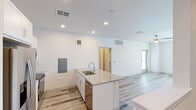 Located at 16230 N Litchfield Road in Surprise, AZ, this thoughtfully designed single-floor unit offers a clean, modern aesthetic with a bright, open layout. The combined kitchen and living area serves as the heart of the space, showcasing a large granite-topped island with an undermount sink — ideal for both meal prep and casual dining. The kitchen is outfitted with crisp white cabinetry, stainless steel appliances including a French door refrigerator, electric range, and over-the-range microwave, all set against a light tile backsplash. Recessed lighting illuminates the space, which flows seamlessly into the living area. Light wood-look flooring runs throughout, contributing to a cohesive and airy feel. A glass-panel exterior door with blinds invites natural light into the living area, complemented by a ceiling fan for added comfort. The bathroom features a granite-topped white vanity with an illuminated frameless mirror, a tub-shower combo, and matching wood-look flooring, maintaining the unit's clean, consistent design language. The laundry area is equipped with a stacked Whirlpool washer and dryer alongside generous built-in shelving and hanging rods, maximizing storage efficiency. Overall, the space exudes a fresh, move-in-ready atmosphere with modern finishes and functional design.