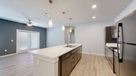 This single-story, 3-bedroom, 2-bathroom home offers a thoughtfully designed open-concept layout with modern finishes throughout. The kitchen and living area form the heart of the home, anchored by a large center island with a white quartz countertop, undermount sink, and sleek pendant lighting overhead. Dark wood cabinetry pairs elegantly with black appliances, while light wood-style vinyl flooring runs seamlessly throughout the entire home. The living room features a bold slate-blue accent wall, ceiling fan, and French doors that invite natural light and provide outdoor access. Each bedroom is generously proportioned, with large windows fitted with blinds, ceiling fans, and neutral tones. The primary bedroom benefits from its own well-sized walk-in closet with built-in wire shelving. The primary bathroom is a standout, featuring a double-sink vanity with dark wood cabinetry, a large frameless glass shower with tile surround, and ample counter space. A dedicated laundry room houses a full-size side-by-side washer and dryer with additional wire shelving above. Three closets throughout the home provide abundant storage. The overall design is clean, contemporary, and move-in ready.