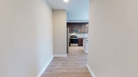 This well-appointed single-floor unit offers a thoughtfully designed open-concept layout with consistent light wood-tone flooring throughout, creating a seamless and cohesive living environment. The kitchen serves as a central highlight, showcasing rich dark walnut cabinetry, granite countertops with subtle speckled detailing, and a full suite of stainless steel appliances including a refrigerator, range, microwave, and dishwasher. Track lighting and elegant pendant fixtures illuminate the space, while a central island with matching granite provides additional prep and gathering space. The living area flows naturally from the kitchen, benefiting from abundant natural light streaming through large windows that frame open outdoor views of the surrounding landscape and skyline. The bedrooms are generously proportioned, each featuring oversized windows that flood the rooms with daylight and offer elevated views of the neighborhood and greenery beyond. The bathroom is finished with the same dark cabinetry found in the kitchen, complemented by a granite-topped vanity, a large mirror, and ample storage. Neutral warm-toned walls throughout the unit contribute to a calm, modern ambiance, making this a well-balanced and functional living space.