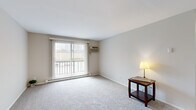 This single-floor residence offers a practical and comfortable layout across two bedrooms, one bathroom, and a collection of well-defined living spaces. The living room is a standout area, featuring plush carpeting, neutral wall tones, and a large sliding glass door with vertical blinds that floods the room with natural light and provides access to an outdoor balcony. A wall-unit air conditioner and baseboard heating ensure year-round comfort in this inviting space.

The kitchen is neatly designed with white shaker-style cabinetry, granite-patterned countertops, a stainless steel sink, and light wood-tone flooring, creating a clean and modern aesthetic. The primary bedroom is generously sized, offering carpet flooring, a ceiling fan with light fixture, and a window overlooking greenery. The second bedroom mirrors this comfortable style with its own ceiling fan and natural light from a window with vertical blinds.

The full bathroom features a tiled tub-and-shower combination, a white vanity with ample storage, and wood-tone flooring. Three closets provide practical storage throughout. A connecting hallway ties all rooms together efficiently, completing this well-organized and move-in-ready home.