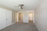 This single-story space is designed with a practical, straightforward layout that accommodates comfortable everyday living. The kitchen is outfitted with white cabinetry, dark laminate countertops, and a double stainless steel sink, complemented by wood-look tile flooring that extends through the kitchen and into adjacent areas. White appliances, including a refrigerator and coil-burner range, provide essential functionality. A doorway from the kitchen leads to a built-in shelving unit, offering convenient additional storage.

The bedrooms are carpeted in neutral tones and feature warm beige walls with white trim throughout. Each room benefits from natural light via horizontal-blind-covered windows, and ceiling fans are present in multiple rooms to support airflow and comfort. Closet space is provided within the bedrooms, and the overall floor plan, visible in the 3D model, illustrates a well-organized arrangement of rooms connected by clear corridors.

The bathroom includes wood-look tile flooring, a white vanity, a full soaking tub with a shower fixture, and a window above the tub that allows natural light into the space. The consistent neutral color palette and clean finishes throughout create a cohesive and functional living environment.