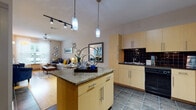 This single-floor residence offers a thoughtfully designed open-concept layout that seamlessly connects the kitchen and living areas. The kitchen is a standout feature, outfitted with light maple cabinetry, a bold black tile backsplash, dark slate-style tile flooring, and a generous granite-topped island that provides both prep space and a natural gathering point. Stainless steel appliances, including a full-size refrigerator and range, complete the functional kitchen setup.

The living area flows naturally from the kitchen, featuring warm hardwood-style flooring, track lighting overhead, and a ceiling fan. Large windows allow ample natural light to fill the space, creating a bright and welcoming atmosphere. A dedicated seating nook provides an additional relaxation area with room for accent chairs and artwork.

The bedroom is carpeted for comfort and includes a ceiling fan, multiple windows with blinds and curtain panels, and generous space for furnishings. The bathroom mirrors the home's design aesthetic with matching light maple cabinetry, dark granite countertops, slate tile flooring, and a well-lit vanity mirror. Throughout the residence, a consistent palette of neutral tones, natural wood finishes, and dark accents creates a cohesive and modern living environment.