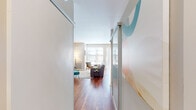 This well-appointed single-floor unit offers a thoughtfully designed layout that balances open living with private spaces. Rich hardwood flooring flows throughout the main areas, anchoring a bright and cohesive aesthetic.

The living area serves as the heart of the space, bathed in natural light from expansive floor-to-ceiling windows and a sliding glass door that opens to an outdoor area. The generous glazing draws in outdoor views and creates an airy, welcoming atmosphere. Sliding frosted-glass partition panels at the entry add a modern architectural touch while providing flexible privacy.

The kitchen is efficiently laid out in an L-shape, featuring wood-grain cabinetry, frosted glass upper cabinets, granite countertops, stainless steel appliances, and a distinctive built-in wine rack — combining style with practical storage.

The bedroom is a calm, understated retreat with soft neutral walls, warm lighting, and direct access to a dedicated closet with built-in shelving and hanging rods. The bathroom continues the clean modern palette, featuring wood-toned cabinetry, a single vanity, and a shower-tub combination. Built-in open shelving provides additional storage. Overall, the space maintains a bright, contemporary feel throughout.