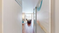 This well-appointed single-floor unit offers a thoughtfully designed layout that balances open living with private spaces. Rich hardwood flooring flows throughout the main areas, anchoring a bright and cohesive aesthetic.

The living area serves as the heart of the space, bathed in natural light from expansive floor-to-ceiling windows and a sliding glass door that opens to an outdoor area. The generous glazing draws in outdoor views and creates an airy, welcoming atmosphere. Sliding frosted-glass partition panels at the entry add a modern architectural touch while providing flexible privacy.

The kitchen is efficiently laid out in an L-shape, featuring wood-grain cabinetry, frosted glass upper cabinets, granite countertops, stainless steel appliances, and a distinctive built-in wine rack — combining style with practical storage.

The bedroom is a calm, understated retreat with soft neutral walls, warm lighting, and direct access to a dedicated closet with built-in shelving and hanging rods. The bathroom continues the clean modern palette, featuring wood-toned cabinetry, a single vanity, and a shower-tub combination. Built-in open shelving provides additional storage. Overall, the space maintains a bright, contemporary feel throughout.