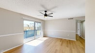 This single-floor unit offers a well-organized layout comprising a living room, kitchen, bedroom, bathroom, and hallway. The living room is a bright, open space highlighted by light hardwood-style flooring, neutral warm-gray walls with a distinctive chair rail detail, and a textured ceiling fitted with a ceiling fan with integrated lighting. A sliding glass door fills the room with natural light and provides direct access to a private balcony with outdoor views, creating an airy and welcoming atmosphere.

The kitchen is efficiently designed, featuring crisp white cabinetry, marble-style countertops, a decorative tile backsplash, and black appliances including a refrigerator, dishwasher, and range. Flush ceiling lighting and matching hardwood-style flooring maintain visual consistency throughout.

The bedroom is a comfortable, well-proportioned space with its own ceiling fan, a natural light-admitting window with blinds, and two closets accessible via a short hallway. The neutral tones and hardwood flooring continue here, offering a calm and cohesive environment.

The bathroom includes a full-size tub-shower combo with white tile surround. Throughout the unit, consistent finishes—neutral paint tones, white trim, and light flooring—create a clean, unified aesthetic.