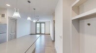 This contemporary 660-square-foot apartment offers a harmonious blend of style and functionality. The heart of the home is an open-concept living area, seamlessly integrating the kitchen and living room. The kitchen boasts crisp white cabinetry, stainless steel appliances, and a striking blue tile backsplash, creating a modern aesthetic. A large island with a quartz countertop provides additional workspace and casual dining options.

The spacious 170-square-foot bedroom features plush carpeting and large windows that flood the space with natural light. French doors in the living area lead to a private outdoor space, perfect for enjoying morning coffee or evening relaxation. The bathroom, while not pictured, likely continues the modern design theme found throughout the apartment.

Light wood flooring in the main living areas adds warmth to the predominantly white color scheme. The apartment's design maximizes space efficiency, with built-in storage solutions and a dedicated entryway area. Recessed lighting and contemporary pendant fixtures provide ample illumination, enhancing the overall bright and airy atmosphere of this stylish urban dwelling.
