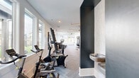 Located at 615 Fallview Ln in Boone, NC, this well-appointed fitness facility spans a generous single floor, offering a comprehensive workout experience in a modern, thoughtfully designed setting. The facility is organized into distinct zones, each tailored to a specific type of training.

The main cardio and strength area is bright and airy, lined with large windows that invite abundant natural light and frame views of the surrounding landscape. Rows of TRUE-brand treadmills, ellipticals, and cycling bikes are arranged along one side, while a full suite of strength machines, free weights, benches, and cable systems occupy the opposing zones. Ceiling fans and linear pendant lighting contribute to a clean, contemporary aesthetic, and herringbone-patterned carpet flooring runs throughout.

A dedicated functional training studio features hardwood floors and a striking nature-inspired mountain mural across its walls. This room is equipped with a multi-use training rig, battle ropes, medicine balls, resistance tools, and TRX suspension systems, creating an immersive space for dynamic, full-body workouts.

An additional exercise area includes televisions, weight storage, and direct access to the outdoors. Outside, a terrace with artificial turf and patio seating overlooks sweeping mountain views, ideal for outdoor training or relaxation. The building's exterior presents a classic white board-and-batten façade with dark trim accents.