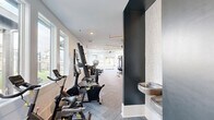 Located at 615 Fallview Ln in Boone, NC, this well-appointed fitness facility spans a generous single floor, offering a comprehensive workout experience in a modern, thoughtfully designed setting. The facility is organized into distinct zones, each tailored to a specific type of training.

The main cardio and strength area is bright and airy, lined with large windows that invite abundant natural light and frame views of the surrounding landscape. Rows of TRUE-brand treadmills, ellipticals, and cycling bikes are arranged along one side, while a full suite of strength machines, free weights, benches, and cable systems occupy the opposing zones. Ceiling fans and linear pendant lighting contribute to a clean, contemporary aesthetic, and herringbone-patterned carpet flooring runs throughout.

A dedicated functional training studio features hardwood floors and a striking nature-inspired mountain mural across its walls. This room is equipped with a multi-use training rig, battle ropes, medicine balls, resistance tools, and TRX suspension systems, creating an immersive space for dynamic, full-body workouts.

An additional exercise area includes televisions, weight storage, and direct access to the outdoors. Outside, a terrace with artificial turf and patio seating overlooks sweeping mountain views, ideal for outdoor training or relaxation. The building's exterior presents a classic white board-and-batten façade with dark trim accents.