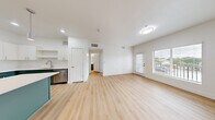 Located in Washington, Utah, this thoughtfully designed one-bedroom, one-bathroom unit offers a clean, modern aesthetic with an efficient and functional layout. The open-concept kitchen and living area serves as the heart of the home, showcasing light wood-tone luxury vinyl plank flooring, crisp white walls, and abundant natural light streaming through large windows with blinds. A private exterior door leads to an outdoor balcony area, extending the living space beyond its walls.

The kitchen is a standout feature, centered around a substantial island with teal-toned cabinetry and a bright white countertop, illuminated by sleek pendant lighting. Upper white cabinetry contrasts stylishly with the teal lower cabinets, and the space is equipped with a full suite of stainless steel appliances, including a refrigerator, gas range, microwave, and dishwasher.

The bedroom offers plush carpeting, a generous window with outdoor views, and a clean, serene atmosphere. The bathroom continues the teal cabinetry theme with a wide vanity, white countertop, and a large mirror with contemporary lighting. A dedicated closet space doubles as a laundry area, complete with a stacked washer and dryer unit and a clothing rod for added convenience.