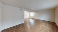 This single-floor unit is finished with warm-toned wood-look flooring that runs consistently throughout the space, creating a cohesive and inviting atmosphere. The living areas are open and well-proportioned, featuring neutral white walls, textured ceilings, and large windows fitted with blinds that allow natural light to fill the rooms. One living space features an angled ceiling detail that adds architectural character and a sense of depth.

The galley-style kitchen is efficiently laid out with dark espresso cabinetry lining both sides, light granite-style countertops, a stainless steel sink, and black appliances including a refrigerator, range, and built-in microwave. A louvered door at the end of the kitchen leads to a utility area housing the electrical panel.

The bedrooms are generously sized, each equipped with sliding panel closets that offer practical built-in storage. Windows in the bedrooms provide natural light and views of surrounding greenery.

The bathroom is clean and functional, featuring a white tub and shower unit with integrated shelving, a toilet, a vanity with granite-style countertop, and wood-look flooring that ties the space together with the rest of the unit.