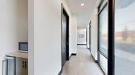 Located at 2504 Bransford Ave in the vibrant Berry Hill neighborhood of Nashville, TN, this modern single-story commercial office space offers a well-designed layout across a generous footprint. The space accommodates 14 rooms thoughtfully arranged to support a variety of professional needs.

The entrance and common area immediately set the tone with dramatic dark-painted walls, large floor-to-ceiling windows, and terrazzo flooring that floods the space with natural light. Vivid red accent chairs and round tulip tables create an inviting lounge atmosphere, while glass doors open directly onto an outdoor patio area — ideal for informal meetings or breaks.

A wide, polished concrete hallway connects the interior rooms, lined with sleek black-framed doors and large windows that maintain a bright, airy feel. A small kitchenette nook along the corridor provides added convenience, outfitted with a microwave and under-counter refrigerator.

Private offices throughout the space are clean and minimalist, featuring built-in desk surfaces, patterned carpet, and ample room for focused individual work. A dedicated conference room offers a spacious boardroom-style setup with a large central table, ergonomic seating for eight or more, a wall-mounted display, and a full-length glass whiteboard — making it well-suited for client presentations and team collaboration. The overall aesthetic is contemporary and professional, balancing functionality with modern design.