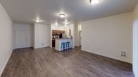 Located at 10436 SE Carr Rd in Renton, Washington, unit B204 is a single-floor residence offering a well-organized layout with distinct living, kitchen, and bedroom areas. The open-concept living and dining area is finished with rich, dark wood-style plank flooring that extends throughout the main living spaces, lending a warm and cohesive aesthetic. Flush-mount ceiling lights illuminate the area evenly, creating a bright and functional environment.

The kitchen is thoughtfully designed with a galley-style configuration featuring warm wood cabinetry, neutral countertops, a double-basin sink, and stainless steel appliances including a refrigerator and microwave. A peninsula with bar-height seating bridges the kitchen to the living area, offering a casual dining option and enhancing the open feel of the space.

The bedrooms are carpeted in neutral tones, providing a softer, quieter retreat from the main living areas. Natural light enters through windows with blinds, and the rooms offer clean white walls with ample space for furnishings. The floor plan, as seen in the 3D overview, reflects a practical arrangement with clear separation between living and private spaces, making the unit functional and easy to navigate throughout.