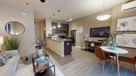 This single-story residence offers a thoughtfully arranged open-concept layout that seamlessly connects the kitchen, dining, and living areas. Light-toned wood-style flooring runs throughout the main living spaces, contributing to a clean, cohesive aesthetic.

The kitchen serves as a functional centerpiece, featuring dark espresso cabinetry, granite countertops, and a peninsula with an integrated sink that opens toward the living area. Stainless steel appliances—including a range, microwave, and refrigerator—are complemented by pendant lighting that illuminates the workspace effectively. A ceiling fan overhead aids in air circulation throughout the open living zone.

The living area is compact yet well-proportioned, with a front entry door featuring a transom window that introduces natural light. The dining space is positioned adjacent to the kitchen, with vertical blinds providing light control along a nearby window.

The bedroom offers a quiet, neutral atmosphere with warm-toned walls, light flooring, and tasteful wall art. The bathroom is efficiently designed, featuring a walk-in glass shower, a dark-cabinetry vanity with a granite countertop, and a large mirror. A hallway connects these private spaces, maintaining a clear separation from the main living area.