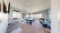 Located at 10602 Burns Rd in Pasco, Washington, this single-floor community game room is a well-appointed recreational space designed to encourage social interaction and leisure. The room is anchored by a full-size pool table with a distinctive light blue felt surface, positioned at the center to maximize accessibility from all areas of the space. Recessed ceiling lighting ensures the area is evenly and adequately illuminated throughout.

Along the perimeter, bar-height bistro tables paired with modern stools provide casual seating for those looking to socialize or take a break between games. A plush sectional sofa with accent pillows and colorful ottoman seating offer a comfortable lounge area, complemented by a wall-mounted flat-screen television. The room is adorned with bold, graffiti-style artwork that adds an urban, energetic character to the space.

A row of large windows along multiple walls allows abundant natural light to fill the room while offering views of the surrounding community. The flooring features a patterned carpet tile layout that adds visual interest and texture underfoot. A vibrant red entry door adds a striking design accent. The overall ambiance is modern, lively, and inviting, making it an ideal gathering space for recreation and community engagement.