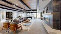 Located in West Valley City, Utah, this single-floor community clubhouse offers a thoughtfully designed gathering space that blends modern style with comfortable amenities. The entrance greets visitors with large floor-to-ceiling windows and glass doors that frame views of the outdoor pool area, flooding the space with natural light and light-toned large-format tile flooring.

The expansive living room is the heart of the space, featuring a striking coffered ceiling with dark wood beams and natural wood paneling that adds warmth and architectural character. A sleek linear gas fireplace set within a dark stone surround and flanked by built-in shelving serves as a dramatic focal point. The open layout accommodates generous seating arrangements and flows seamlessly into a game area complete with a full-size billiard table, pendant lighting, and oversized windows overlooking the pool and courtyard.

The modern kitchen is outfitted with rich dark cabinetry, a mosaic tile backsplash, stainless steel appliances including a French door refrigerator and dishwasher, open shelving, and light tile flooring — ideal for catering and resident events.

Throughout the space, curated artwork, indoor greenery, and carefully selected furnishings contribute to a polished, welcoming ambiance that balances contemporary design with everyday comfort.