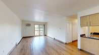 Located at 31 Olympic Village in Chicago Heights, IL, this two-bedroom, one-bathroom residence offers a well-organized single-floor layout with consistent hardwood-style flooring throughout every room, creating a clean and cohesive aesthetic.

The combined living and dining area serves as the heart of the home, offering generous open space bathed in natural light from a sliding glass door that leads directly to a private balcony with outdoor views. A wall-mounted air conditioning unit provides in-unit climate control, and a baseboard heating system runs along the perimeter walls.

The kitchen features light wood cabinetry with ample upper and lower storage, dark countertops, a gas range, and a sink — all efficiently arranged along one wall with open space for a dining setup adjacent to it.

Both bedrooms are comfortably sized, with the primary bedroom offering notably more space. Each bedroom features the same hardwood-style flooring, white walls, and louvered bi-fold closet doors. In total, the unit includes four closets, providing excellent storage capacity throughout.

The bathroom includes a single-sink vanity with wood cabinetry, a mirrored medicine cabinet, a tiled shower-tub combination, and hardwood-style flooring, maintaining design continuity with the rest of the home. The overall ambiance is bright, clean, and functional.