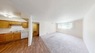 This 2-bedroom, 1-bathroom single-floor unit offers a practical and well-organized layout across a comfortable footprint. The open living room is a highlight of the space, featuring a large picture window that fills the area with natural light and offers views of surrounding greenery. The living room features a combination of hardwood-style flooring and plush carpeting, creating a warm and inviting atmosphere.

Adjacent to the living room, the kitchen is outfitted with warm honey-toned wood cabinetry, white appliances including a refrigerator, range, and dishwasher, and a ceiling fan with light fixture overhead. The L-shaped layout provides ample counter space and storage, making it a functional area for everyday cooking.

The primary bedroom is generously sized, featuring soft carpet flooring, neutral white walls, and a window with vertical blinds that allows in natural light. The second bedroom, though more compact, also features hardwood-style flooring and clean white walls, offering versatility as a guest room or home office.

The full bathroom is clean and straightforward, featuring a full-sized tub and shower combo with classic white square tile surround and tiled flooring. A connecting hallway ties all rooms together efficiently, completing this well-structured and move-in ready unit.