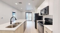 Located at 630 E Main Ave in Bismarck, ND, this efficiently designed one-bedroom, one-bathroom unit delivers a clean, modern aesthetic throughout. The open-concept living and kitchen area anchors the space, centered around a sleek kitchen island with a double stainless steel sink and light wood cabinetry. The kitchen is well-appointed with white upper cabinets, subway tile backsplash, and a full suite of black appliances including a refrigerator, electric range, and over-the-range microwave. Recessed lighting illuminates the space, while a sliding glass door at the end of the kitchen allows natural light to pour in and provides access to an outdoor area. Light hardwood-style flooring flows consistently throughout the entire unit, contributing to a bright and cohesive feel. The bedroom is a compact, well-lit room featuring a large window with a black-framed rail detail, offering views of the surrounding neighborhood and filling the room with natural light. A dedicated closet provides convenient storage. The bathroom maintains the unit's clean design language, with light wood-toned flooring, a single vanity with mirror, a soaking tub, and matte black fixtures as refined accent details throughout.