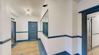 The Pasadena Apartments presents a thoughtfully designed first floor that blends classic architectural character with contemporary updates. The main lobby serves as the building's central hub, featuring light wood-look flooring, bold blue-trimmed doors, and a branded entry mat positioned in front of two elevator bays with striking dark stone-patterned doors. A sputnik-style ceiling fixture adds a modern touch, while a wall-mounted mailbox station provides resident convenience nearby.

The corridors extend from the lobby in a long, well-lit configuration, lined with numbered unit doors finished in a coordinated steel-blue tone with gold hardware. Continuous linear ceiling lighting illuminates the hallways, which feature white walls accented by a blue chair rail and matching baseboards, creating a polished and consistent aesthetic throughout.

The leasing office exudes a welcoming, professional atmosphere, complete with light hardwood flooring, natural light from traditional windows, and a reception counter positioned at the entrance. A standout feature is a large sepia-toned mural depicting the historic Pasadena building, lending a sense of heritage and identity to the space. The office also includes workstations and a secondary room, supporting daily management operations efficiently.