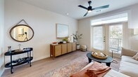 Located at 15506 Interplace Rd in San Antonio, TX, this thoughtfully designed one-bedroom, one-bathroom residence offers a cohesive and modern living experience across a single floor. The open-concept kitchen and living area forms the heart of the home, where white shaker cabinetry, grey subway tile backsplash, quartz countertops, and stainless steel appliances—including a French door refrigerator and range with microwave—create a sleek, functional space. A central island with an undermount sink and pendant lighting doubles as a dining and prep area, making the kitchen as practical as it is attractive. The living room flows naturally from the kitchen, featuring light wood-style flooring, a ceiling fan with integrated lighting, and French doors that invite natural light and outdoor views. The bedroom offers a comfortable retreat with plush carpeting, a ceiling fan, and a generous window framing lush greenery. An adjacent walk-in closet provides ample storage with multiple hanging rods and shelving. The bathroom is well-appointed with a wide quartz vanity, a large framed mirror, wood-look flooring, and a full tiled tub-shower combination. Neutral warm tones and clean lines throughout give this residence a cohesive, contemporary ambiance.