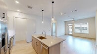 Located at 1345 14th St in Plano, TX, this single-story 2-bedroom, 1-bathroom residence offers a well-designed layout with modern finishes throughout. The open-concept kitchen and living area serves as the heart of the home, showcasing light wood-look flooring, recessed lighting, and a large central island with a white quartz countertop, undermount sink, and pendant lighting above. The kitchen features flat-front cabinetry in a warm wood tone with matte black hardware, a white tile backsplash, and a full suite of stainless steel appliances including a French door refrigerator. The primary bedroom offers hardwood-style flooring, a ceiling fan, and a private exterior door with transom window for added natural light, along with access to a spacious walk-in closet equipped with double hanging rods and built-in shelving. The second bedroom is carpeted and bright, with a large window and ceiling fan. The bathroom is finished with marble-look tile flooring, a wide vanity with blue-gray cabinetry, white countertops, black fixtures, and a large mirror. A dedicated laundry area with wire shelving and a hallway connecting the rooms complete this thoughtfully laid-out home.