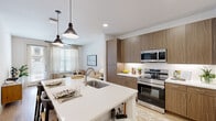 This thoughtfully designed one-bedroom, one-bathroom residence showcases a contemporary open-concept layout that maximizes its efficient footprint. The combined kitchen and living area serves as the heart of the home, featuring light hardwood-style flooring, recessed lighting, and large windows dressed with sheer linen curtains that invite generous natural light. The kitchen is a standout, equipped with stainless steel appliances including a French door refrigerator, electric range, and built-in microwave. Warm wood-toned cabinetry extends floor to ceiling, complemented by crisp white quartz countertops. A central island with an undermount sink doubles as a breakfast bar with seating, making it ideal for casual dining and entertaining. The living area offers a comfortable, bright retreat with a glass-paneled exterior door providing additional light and outdoor access. The bedroom is a serene space featuring plush carpeting, a ceiling fan, and a window with views, creating a calm atmosphere. It connects directly to the well-appointed bathroom, which includes wood-toned vanity cabinetry, a large mirror, and a shower. A dedicated closet provides practical storage, completing this efficiently planned and stylishly finished residence.
