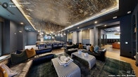 Located at 313 Liggett Street in Durham, NC, this sophisticated clubroom is a generously sized, single-floor amenity space designed with a bold, upscale aesthetic throughout. The interior is anchored by a dramatic central lounge featuring deep navy walls, richly textured metallic ceiling treatments, and a striking rope-and-pendant light installation that cascades overhead. Plush leather sofas, striped upholstered coffee tables, and layered area rugs create an inviting social atmosphere. A long communal bar island with cushioned bar seating sits beneath the decorative ceiling feature, complemented by marble-topped accent tables and warm wood flooring. An adjacent kitchen-style area offers a white countertop bar, built-in appliances, green subway tile accents, and a large wall-mounted display screen. Toward the entry, cognac leather armchairs are arranged around a low coffee table beneath a sculptural sputnik chandelier, with access to glass-walled private rooms outfitted for focused work or meetings. A cozy nook tucked into the wall features channel-tufted green velvet seating beneath a geometric wall panel, alongside a dedicated coffee and refreshment station. Textured wood mosaic wall panels and dark tile flooring add depth and warmth throughout the transitional corridors, making this clubroom a cohesive blend of comfort, function, and contemporary design.
