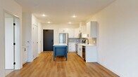 Located at 11900 Wayzata Blvd in Minnetonka, MN, this well-appointed one-bedroom, one-bathroom unit offers a thoughtfully designed open-concept layout across a single floor. The combined living, dining, and kitchen area serves as the heart of the home, anchored by a modern kitchen outfitted with crisp white shaker cabinetry, a neutral tile backsplash, stainless steel appliances including a refrigerator, range, and microwave, and a central island with a white countertop that doubles as a dining and prep space. Light wood-tone flooring runs throughout the main living areas, contributing to a clean, contemporary aesthetic. The living area is bright and open, with a sliding glass door leading to a private balcony that offers views of the surrounding landscape and greenery. The bedroom features soft carpeting, large black-framed windows with outdoor views, and ample natural light. Three closets provide generous storage throughout the unit. The bathroom is finished with a white vanity, undermount sink, and a full tub-shower combination with tile surround. A dedicated laundry area adds everyday convenience. The overall design is modern and cohesive, with a neutral palette and clean finishes throughout.