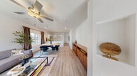 Located at 6931 Plentiful Springs Ct in Las Vegas, NV, this two-story home offers a thoughtfully designed layout spread across two floors. The main level opens into a bright, open-concept living area where light wood-look flooring, crisp white walls, and ceiling fans create a clean, welcoming atmosphere. A warm wood credenza anchors the living space, which flows seamlessly into a dining area and a well-appointed kitchen. The kitchen features an expansive white quartz island with an undermount sink, white shaker cabinetry, and stylish pendant lighting overhead. A staircase with a tall vertical window floods the entry with natural light, connecting the two levels. Upstairs, the generously sized primary bedroom offers plush carpeting, a ceiling fan, and natural light from well-placed windows. A second bedroom provides comparable comfort and bright neighborhood views. Five bathrooms serve the home throughout, including a sleek full bath with a wide double-vanity, white cabinetry, and large mirror. A dedicated office on the upper floor features carpet flooring, a ceiling fan, and a sliding glass door with exterior views—ideal for remote work. Three closets and a hallway complete the upper level, offering ample storage throughout this well-organized Las Vegas home.