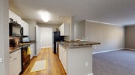 This 2-bedroom, 2-bathroom residence at MAA Berkeley Lake in Duluth, Georgia, presents a thoughtfully designed single-floor layout that balances comfort and functionality. The open-concept living and dining area is generously proportioned, featuring plush carpeting, crown molding, and a seamless connection to the kitchen via a breakfast bar peninsula. The kitchen is well-equipped with white cabinetry, dark granite-style countertops, hardwood-style flooring, and black appliances including a refrigerator, range, and dishwasher. A galley-style layout maximizes counter and storage space throughout. Both bedrooms are carpeted and offer natural light through large windows with views of the surrounding greenery, providing a bright and comfortable retreat. Each bathroom is finished with white vanity cabinetry, granite-style countertops, hardwood-style flooring, and a shower-tub combination. Neutral-toned walls throughout the residence create a clean, versatile backdrop. A carpeted hallway connects the private bedroom wing to the main living areas, and the overall layout ensures a smooth, logical flow throughout the home. The consistent use of warm wood tones and neutral finishes lends a cohesive, welcoming ambiance to the entire space.