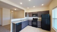 This single-story residence at Windhurst Park offers a thoughtfully designed layout with a clean, modern aesthetic throughout. The kitchen serves as a functional centerpiece, featuring dark espresso-toned cabinetry with ample upper and lower storage, granite-style countertops, and a full suite of black appliances including a refrigerator, range, built-in microwave, and dishwasher. Light wood-look flooring runs through the kitchen, which also benefits from recessed lighting and a door providing direct outdoor access alongside a window that draws in natural light. A breakfast bar-style counter connects the kitchen to the living area, creating an open, communicative flow between spaces.

The living area is generously sized, finished with plush carpet and a ceiling fan overhead. Bedrooms continue the carpeted flooring and ceiling fan combination, with windows offering outdoor views. A dedicated laundry room includes washer and dryer hookups, wire shelving, and tile flooring for practicality. The bathroom features a tub-shower combination, a granite-style vanity countertop with an undermount sink, a large mirror, and matching tile flooring, completing a cohesive and functional interior.