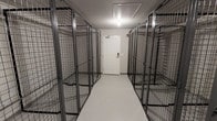 This single-floor storage space is designed with functionality and security as its primary focus. A central corridor runs the length of the room, flanked on both sides by floor-to-ceiling wire mesh storage cages constructed from durable dark metal framing. Each individual unit features its own lockable door, providing secure, separated storage for multiple users within a shared space.

The interior maintains a clean, no-frills aesthetic with white walls and a smooth, light-colored floor that enhances visibility throughout the corridor. Overhead, recessed flush-mount lighting provides consistent, even illumination across the entire space, ensuring clear sightlines from one end to the other.

The corridor terminates at a solid white access door equipped with a keypad or electronic locking mechanism, reinforcing the security-conscious design of the facility. A fire alarm is also visible near the exit, indicating the space meets safety code requirements.

Overall, the space is well-organized and efficiently laid out, maximizing the number of individual storage units while maintaining comfortable access along the central walkway. It is well-suited for multi-tenant residential buildings or commercial facilities requiring shared, secured storage solutions.