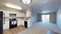 Located in Vancouver, WA, this single-floor, 2-bedroom, 2-bathroom residence offers a practical and comfortable layout. The living room is spacious and carpeted, featuring neutral gray walls and a sliding glass door that fills the space with natural light while providing outdoor access. The kitchen is well-appointed with white cabinetry, light countertops, wood-look vinyl flooring, and black appliances including a range, refrigerator, and dishwasher, all illuminated by overhead lighting. Both bedrooms are carpeted and finished with neutral tones, each featuring sliding closet doors that maximize floor space. Windows in each bedroom allow for natural light and views of the surrounding greenery. The two bathrooms are consistently designed with wood-look vinyl flooring, white cabinetry, taupe countertops, large vanity mirrors, and tub-shower combinations with tile surrounds. A connecting hallway ties the layout together efficiently. Baseboard heating is present throughout the unit. The overall aesthetic is clean and understated, with a neutral color palette that creates a calm, move-in-ready environment suitable for a variety of living arrangements.