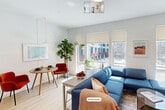 This efficiently designed single-floor unit offers a thoughtfully organized layout that maximizes every square foot. The open-plan living, dining, and kitchen area forms the heart of the space, finished in a crisp white palette with light hardwood flooring that unifies the zones seamlessly. The living area benefits from a bank of large windows that frame outdoor views and flood the space with abundant natural light, creating an airy, bright atmosphere despite the compact footprint.

The kitchen is outfitted with stainless steel appliances, including a built-in refrigerator nestled within floor-to-ceiling white cabinetry, an electric range with an over-range microwave, and a clean white tile backsplash. The cabinetry provides generous vertical storage, keeping the kitchen organized and visually streamlined.

The dining area, positioned near the windows, accommodates an intimate seating arrangement and benefits directly from the natural light and outdoor views. A pendant light overhead adds a warm, functional focal point to the zone.

The bathroom features a full tub-and-shower combination with large-format neutral tile surround, offering a clean, modern finish. Throughout the unit, the consistent white walls, recessed lighting, and light wood floors contribute to a cohesive, contemporary aesthetic.