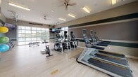 Located at 750 5th St in Oswego, Illinois, this well-appointed fitness center offers a comprehensive workout environment designed to accommodate a wide range of exercise routines. The single-floor space is open and airy, featuring light wood-style flooring, high ceilings with ceiling fans, and generous recessed and overhead lighting that keeps the environment bright and energizing throughout. Large garage-style and standard windows line the walls, flooding the interior with natural light and providing pleasant outdoor views of the surrounding greenery.

The cardio zone is prominently featured, housing a row of Matrix-brand treadmills, multiple elliptical trainers, and stationary cycling bikes — all equipped with individual screens for an engaging workout experience. A dedicated free weights area includes a full rack of dumbbells and a tiered kettlebell stand, complemented by floor-to-ceiling mirrors that visually expand the space and support proper form. Wall-mounted flat-screen TVs are positioned throughout for entertainment.

A wellness station adds a thoughtful touch, featuring shelving with plants, a mini-refrigerator, and a chalkboard menu display — ideal for post-workout refreshment. Stability balls and resistance accessories are neatly organized along the walls. The overall ambiance is clean, modern, and motivating, making this fitness center a fully functional destination for daily training.