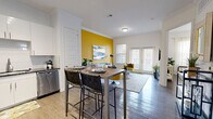 This thoughtfully designed 1-bedroom, 1-bathroom unit offers an efficient and stylish layout across a single floor. The open-concept kitchen and living area serves as the heart of the space, featuring dark hardwood-style flooring, crown molding, and abundant natural light from large windows and French doors. The kitchen is equipped with stainless steel appliances — including a refrigerator, microwave, and dishwasher — complemented by crisp white cabinetry, a tile backsplash, and a built-in dining bar with seating. A bold golden-yellow accent wall anchors the living area, adding a vibrant focal point and visual warmth to the otherwise neutral palette. The bedroom is a serene retreat with windows that invite natural light, continuing the dark hardwood flooring, and direct access to a walk-in closet outfitted with built-in shelving and hanging rods. The full bathroom features a dark granite vanity countertop, white cabinetry, and a soaking tub with shower. Additional conveniences include a dedicated laundry area and pantry storage. Crown molding throughout and track lighting in the kitchen add refined architectural detail to the overall design.