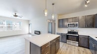 Located in Colorado Springs, CO, this well-appointed 2-bedroom, 2-bathroom single-floor residence offers a thoughtfully designed open-concept layout. The kitchen is a standout feature, showcasing rich dark-toned cabinetry, a large center island with a bright white quartz countertop, stainless steel appliances, and stylish pendant lighting — all flowing seamlessly into the living area. The living room is bathed in natural light from oversized windows and features light hardwood-style flooring, a sleek fireplace, ceiling fan, and a private exterior door. Both bedrooms are comfortably sized, carpeted for warmth, and equipped with ceiling fans and windows that bring in natural light. The primary bedroom includes a spacious walk-in closet with wire shelving for ample storage. The bathrooms are finished with dark wood vanities, white countertops, and a wide LED-backlit mirror in the primary bath, which also features a dual-sink vanity and a full tub-shower combo. A connecting hallway and two closets round out the floor plan. The consistent use of light tones, modern fixtures, and quality materials throughout gives this residence a clean, contemporary feel.