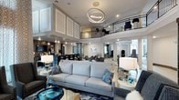 Located at 4800 Marriott Dr in Raleigh, NC, this single-floor space presents a grand, open-concept layout with impressive double-height ceilings that create an expansive, airy atmosphere. A curved mezzanine level with a sleek black metal railing overlooks the main floor below, adding architectural drama and visual depth to the interior.

The main gathering area is anchored by a substantial light gray sofa ensemble, accented with blue and gray throw pillows that complement the rich navy and teal-toned area rug beneath. A statement circular LED chandelier suspended from the ceiling serves as a striking focal point, casting a warm, modern glow throughout the space. Pendant lighting fixtures are distributed throughout, adding layered illumination.

The open layout flows seamlessly into multiple functional zones, including lounge seating areas and what appears to be a reception or service counter in the background. Decorative columns define spatial transitions without interrupting the open feel. The overall design palette of soft grays, whites, and bold blue accents conveys a polished, contemporary aesthetic suited for a professional or hospitality environment.