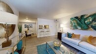 This single-floor residence offers a thoughtfully designed layout that balances open communal spaces with private quarters. The living room serves as the heart of the home, featuring wood-look flooring, a teal accent rug, and a large sliding glass door with vertical blinds that opens to a private balcony, allowing natural light to fill the space. Vibrant wall art in teal and gold tones enhances the contemporary aesthetic throughout.

The galley-style kitchen is efficiently organized with gray shaker cabinetry, light quartz-style countertops, and a full suite of stainless steel appliances, including a refrigerator, electric range, microwave, and dishwasher. A pass-through counter with bar seating connects the kitchen to the main living area. Adjacent to the living room, a defined dining nook accommodates a four-seat table beneath overhead lighting.

Both bedrooms feature plush carpeting and ceiling-mounted fixtures, with one room offering a ceiling fan and the other showcasing a tufted headboard aesthetic. The bathroom includes a wide vanity with granite-style countertops, a large mirror, and clean, neutral finishes throughout.