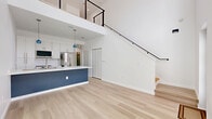 Located at 527 N Garden Ave in Clearwater, FL, this contemporary two-story home delivers a clean, modern aesthetic with high-end finishes throughout. Light wood flooring flows seamlessly across both levels, complementing the crisp white walls and abundant natural light that fills the space.

The main floor features a striking open-concept kitchen with white shaker cabinetry, a bold navy-blue island base topped with a sleek quartz countertop, stainless steel appliances, and a professional-style faucet. Two blue pendant lights add a stylish accent above the island. Soaring ceilings with an open mezzanine view above create a dramatic sense of vertical space in the living area.

A modern staircase with matte black cable railings leads to the upper level, where an open loft-style landing is bathed in natural light from multiple windows and cooled by dual ceiling fans. The bedroom offers a serene, minimalist retreat with a closet featuring louvered bifold doors and a window framing outdoor greenery.

Both bathrooms are refined and spa-like. One features full marble-style tile walls, a frameless glass walk-in shower with a rain showerhead, mosaic tile flooring, and a navy vanity with brushed nickel hardware. Additional highlights include multiple closets, a laundry area, and a basement for extra utility.