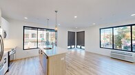 This thoughtfully designed 2-bedroom, 2-bathroom single-floor residence offers a clean, contemporary aesthetic throughout. The open-concept kitchen and living area serves as the heart of the unit, anchored by a light wood-toned island with a white quartz countertop, stainless steel appliances, white cabinetry, and stylish pendant lighting. Large black-framed windows flood the space with natural light and provide views of the surrounding neighborhood streetscape. Light hardwood flooring runs seamlessly throughout, enhancing the bright, airy atmosphere.

The spacious living area extends naturally from the kitchen, with multiple oversized windows fitted with roller shades, offering both openness and privacy. Each bedroom is well-proportioned, featuring large windows with street views, recessed lighting, and wall-mounted HVAC units. The primary bedroom includes generous closet space with double doors. Both bathrooms are finished in a clean, modern style with large-format tile flooring, a wood-toned vanity, white countertops, and a full soaking tub with shower. A central hallway connects all rooms efficiently, completing this well-appointed and move-in ready residence.