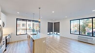 This thoughtfully designed 2-bedroom, 2-bathroom single-floor residence offers a clean, contemporary aesthetic throughout. The open-concept kitchen and living area serves as the heart of the unit, anchored by a light wood-toned island with a white quartz countertop, stainless steel appliances, white cabinetry, and stylish pendant lighting. Large black-framed windows flood the space with natural light and provide views of the surrounding neighborhood streetscape. Light hardwood flooring runs seamlessly throughout, enhancing the bright, airy atmosphere.

The spacious living area extends naturally from the kitchen, with multiple oversized windows fitted with roller shades, offering both openness and privacy. Each bedroom is well-proportioned, featuring large windows with street views, recessed lighting, and wall-mounted HVAC units. The primary bedroom includes generous closet space with double doors. Both bathrooms are finished in a clean, modern style with large-format tile flooring, a wood-toned vanity, white countertops, and a full soaking tub with shower. A central hallway connects all rooms efficiently, completing this well-appointed and move-in ready residence.
